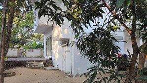 A white building with a small porch and a sandy ground area.
