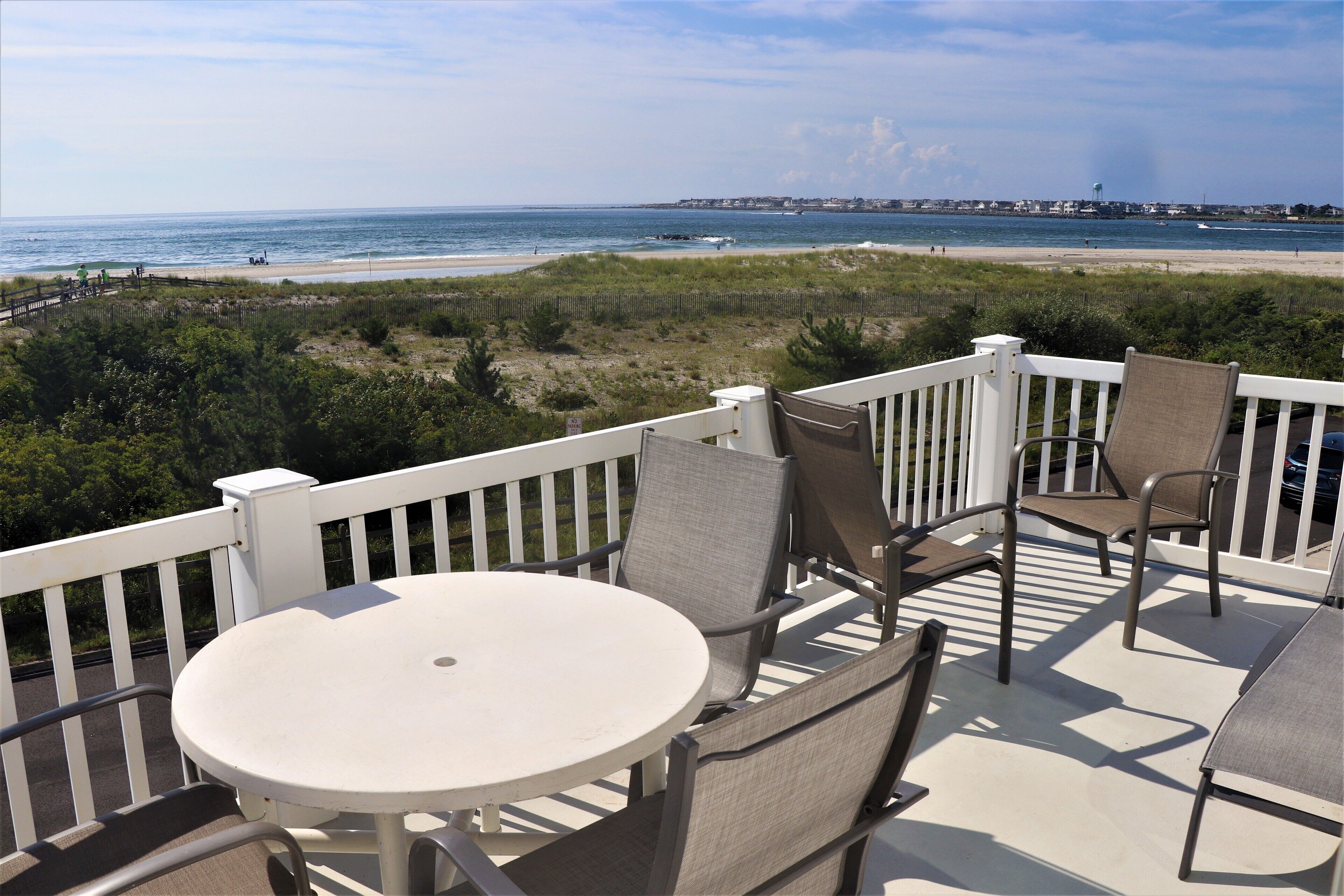 A deck with a round table and chairs, overlooking a beach with a fence and vegetation.