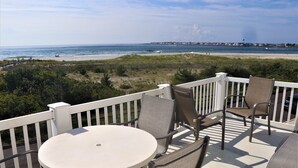 Una terrazza con un tavolo rotondo e sedie, affacciata su una spiaggia con una recinzione e vegetazione.