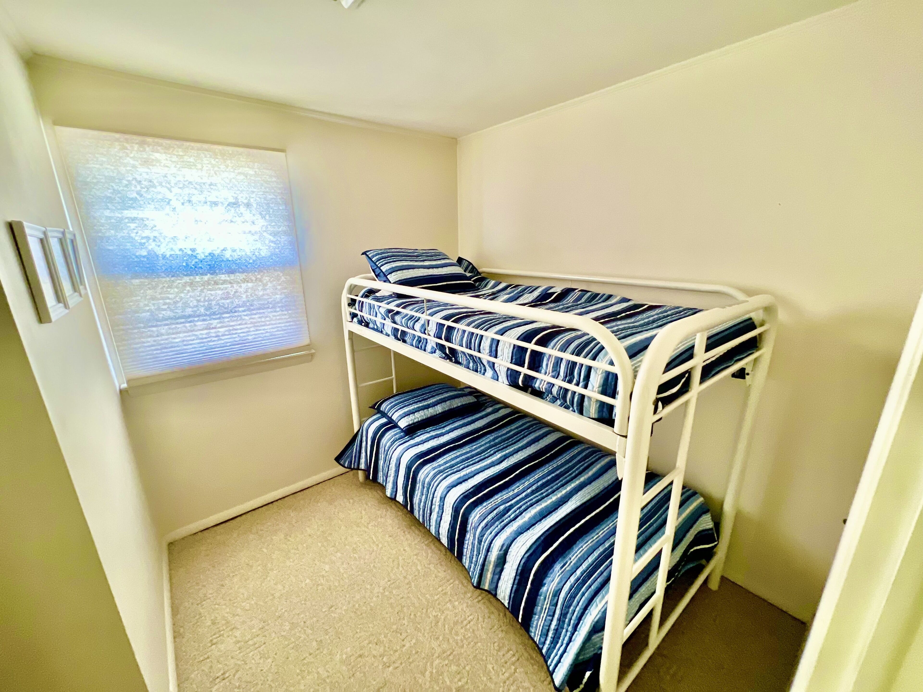 Een stapelbed met gestreepte dekens in een kleine kamer met een raam.
