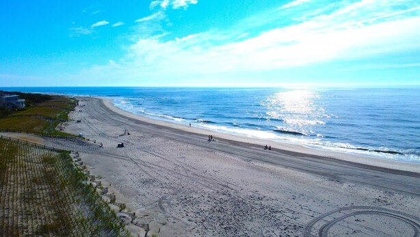 Una spiaggia costiera con cielo sereno, una battigia sabbiosa e alcune persone che passeggiano.
