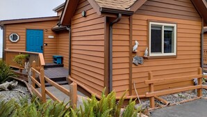 Un bâtiment en bois avec une porte bleue, un petit porche et une fenêtre ornée d’un motif représentant un pélican.