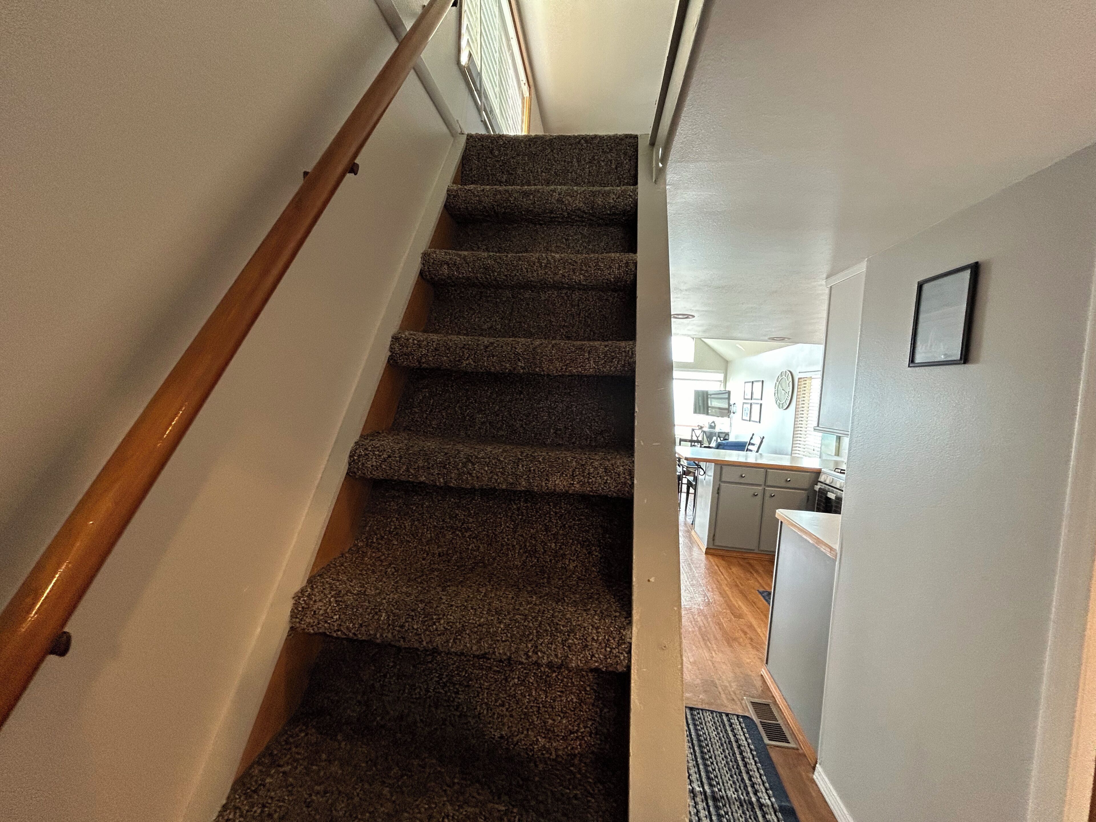 Una escalera alfombrada con barandilla de madera que conduce a una zona de cocina con una mesa y sillas.