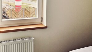 A room with a window overlooking a lighthouse, a radiator, and a bed. - Apartments Möwe - Apartment upper floor with lake view (Lembruch)