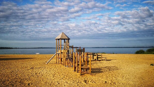 A beach with a wooden play structure and a lookout tower. - Apartments Möwe - Apartment upper floor with lake view (Lembruch)