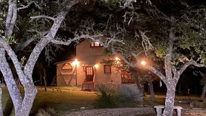 A house with a porch, a small window, and a door, surrounded by trees. - Amish cabin at Wolf Creek Guest Ranch (Fredericksburg)