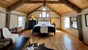 A spacious room with a high wooden ceiling, a large bed, a sofa, and a cowhide rug. - Amish cabin at Wolf Creek Guest Ranch (Fredericksburg)