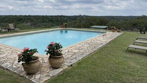 A rectangular pool with a stone border, surrounded by a grassy area and potted plants. - Amish cabin at Wolf Creek Guest Ranch (Fredericksburg)