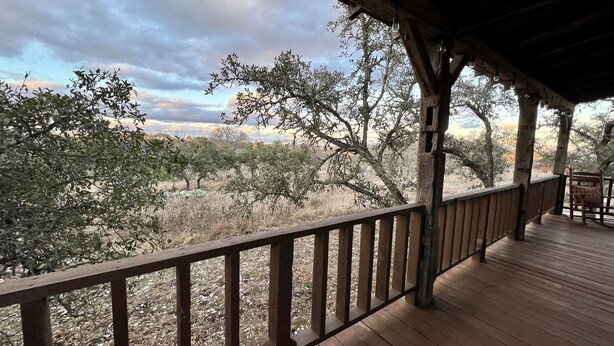 A wooden deck with a railing overlooking a dry landscape with sparse trees and shrubs. - Amish cabin at Wolf Creek Guest Ranch (Fredericksburg)