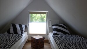 Een kleine zolderkamer met twee bedden, een raam en een radiator.