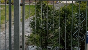 Een wit gebouw met een rood dak, groene luiken en een metalen hek in de voorgrond.