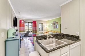 A compact kitchen with a sink, a coffee maker, and a dining area with chairs and a table.