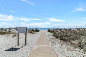 A sandy beach path leading to the ocean with a signpost on the left.