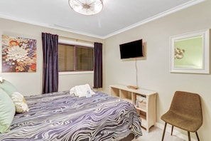 A hotel room with a bed, a desk, a chair, a television, and artwork on the walls.