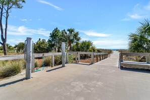A wooden boardwalk leading to a beach with metal railings and trees.