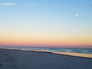 A beach with a clear sky and a visible moon.