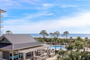 A beachfront hotel with a pool, outdoor seating, and a view of the ocean.