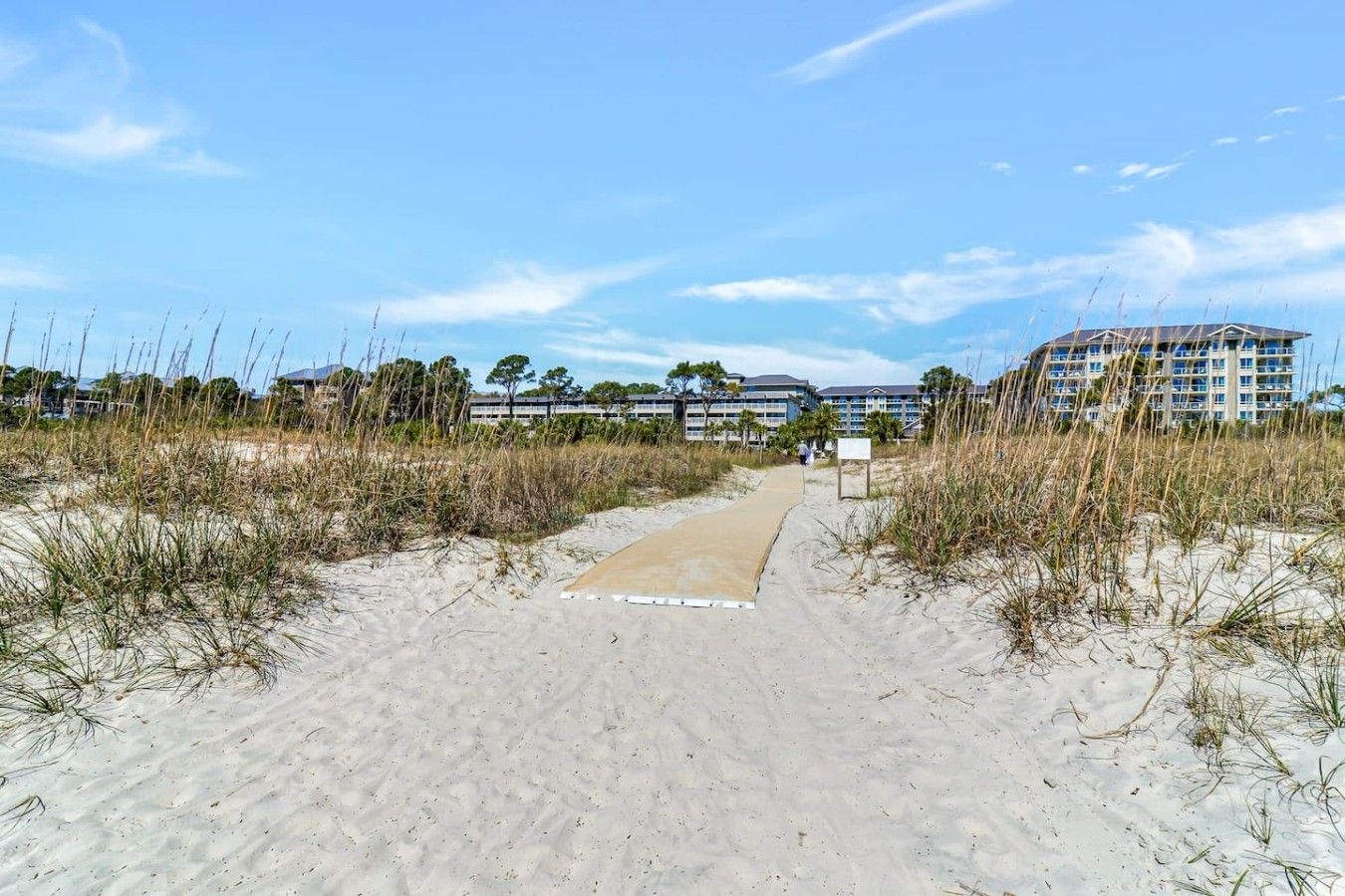 A sandy pathway leading to a beachfront hotel with multiple stories and a clear sky.