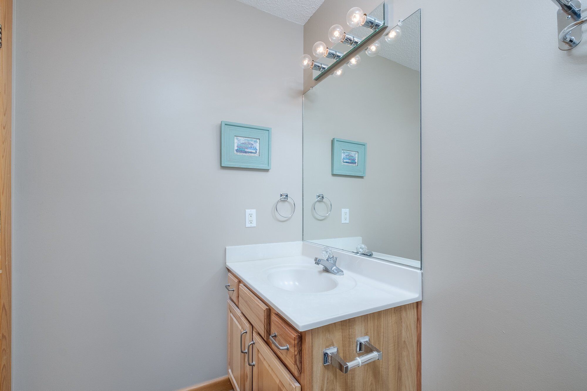 A bathroom with a white sink, wooden cabinets, a large mirror, and two framed pictures on the wall.
