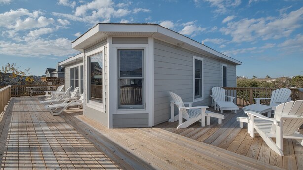 Eine überdachte Terrasse im Freien mit weißen Adirondack-Stühlen und einem kleinen Gebäude mit großen Fenstern.