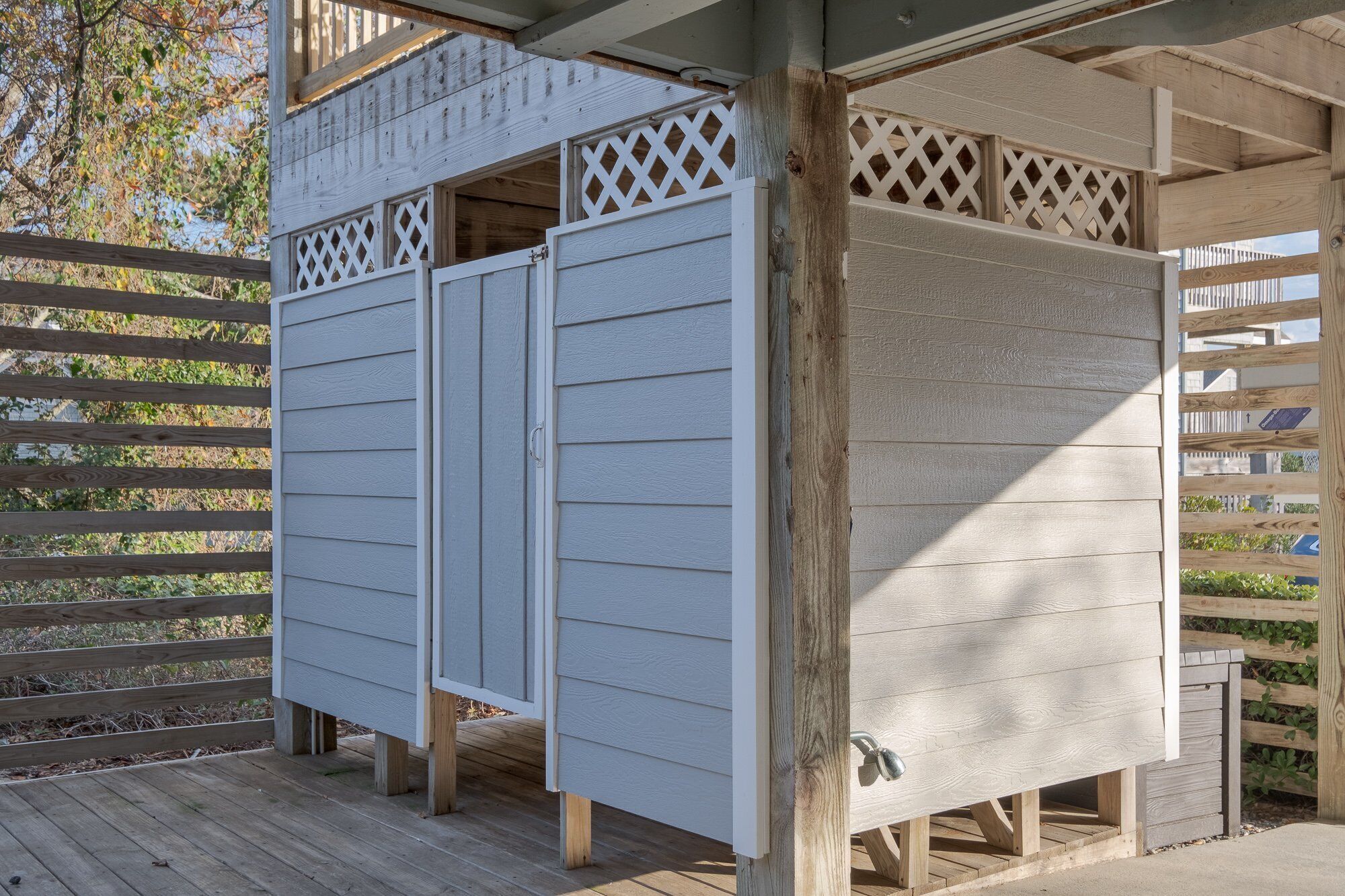 A covered outdoor area with a wooden deck, a white building with a lattice window, and a wooden fence.