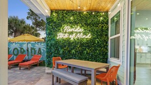 An outdoor patio with a wooden table, orange chairs, and a bench. A neon sign reads "Florida State of Mind." - Resort Pool Oasis • Game Room • Walk to Beach • Sleeps 15 (Panama City Beach)