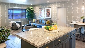 A modern kitchen with granite countertops, a dining area with a bar, a seating area with a sofa and coffee table, and a large window with a view.