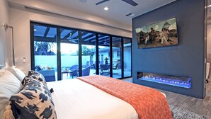 A modern bedroom with a large bed, a fireplace, and a sliding glass door leading to an outdoor patio.