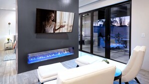 A modern living room with a flat-screen TV, a built-in fireplace, and a seating area with white leather chairs.
