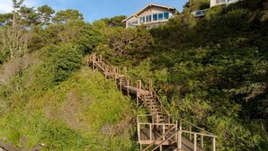 A wooden staircase leading to a house surrounded by dense greenery. - Panoramic Promontory: Bay View Beach House (Waldport)