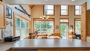 Une cuisine spacieuse, dotée de meubles en bois, d’un grand îlot central et de nombreuses fenêtres offrant une vue sur l’extérieur.