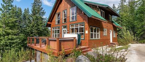 A wooden cabin with a green roof, multiple windows, and a deck.