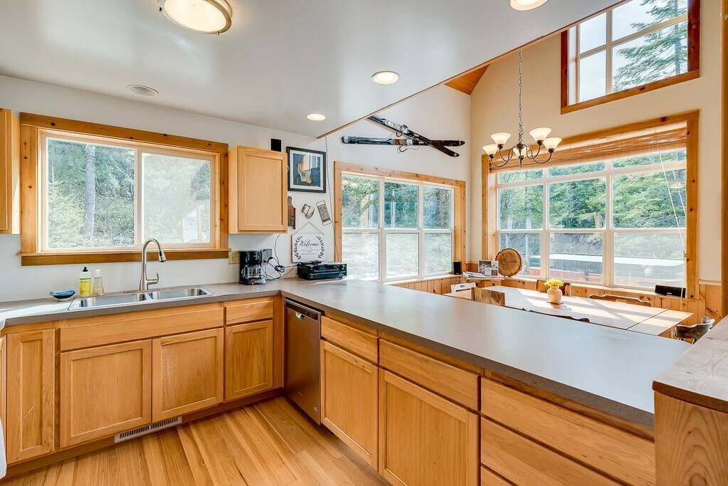 A modern kitchen with wooden cabinets, a large island, and large windows offering views of the outdoors.