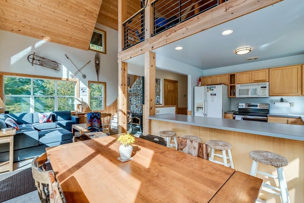 A spacious living area with a wooden dining table, a sofa, and a kitchen with wooden cabinets and a microwave.