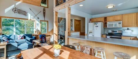 A spacious living area with a wooden dining table, a sofa, and a kitchen with wooden cabinets and a microwave.