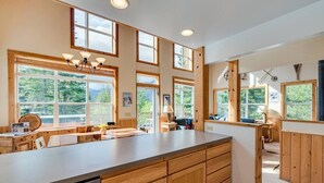 Une cuisine spacieuse, dotée de meubles en bois, d’un grand îlot central et de nombreuses fenêtres offrant une vue sur la verdure.