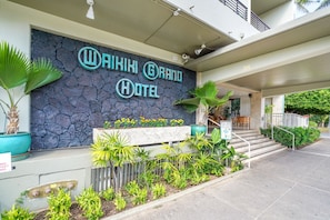 Welcome to the Waikiki Grand Hotel, where lush greenery surrounds the entrance, featuring a bar and staircase.