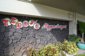 Sign for Tendo's Bigger Burgers against a stone wall, accompanied by a potted plant.