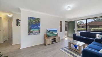A living room with a TV, a blue couch, and a painting of a beach scene.