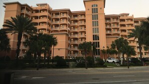 Un hôtel à plusieurs étages doté de balcons, de palmiers et d’un parking.