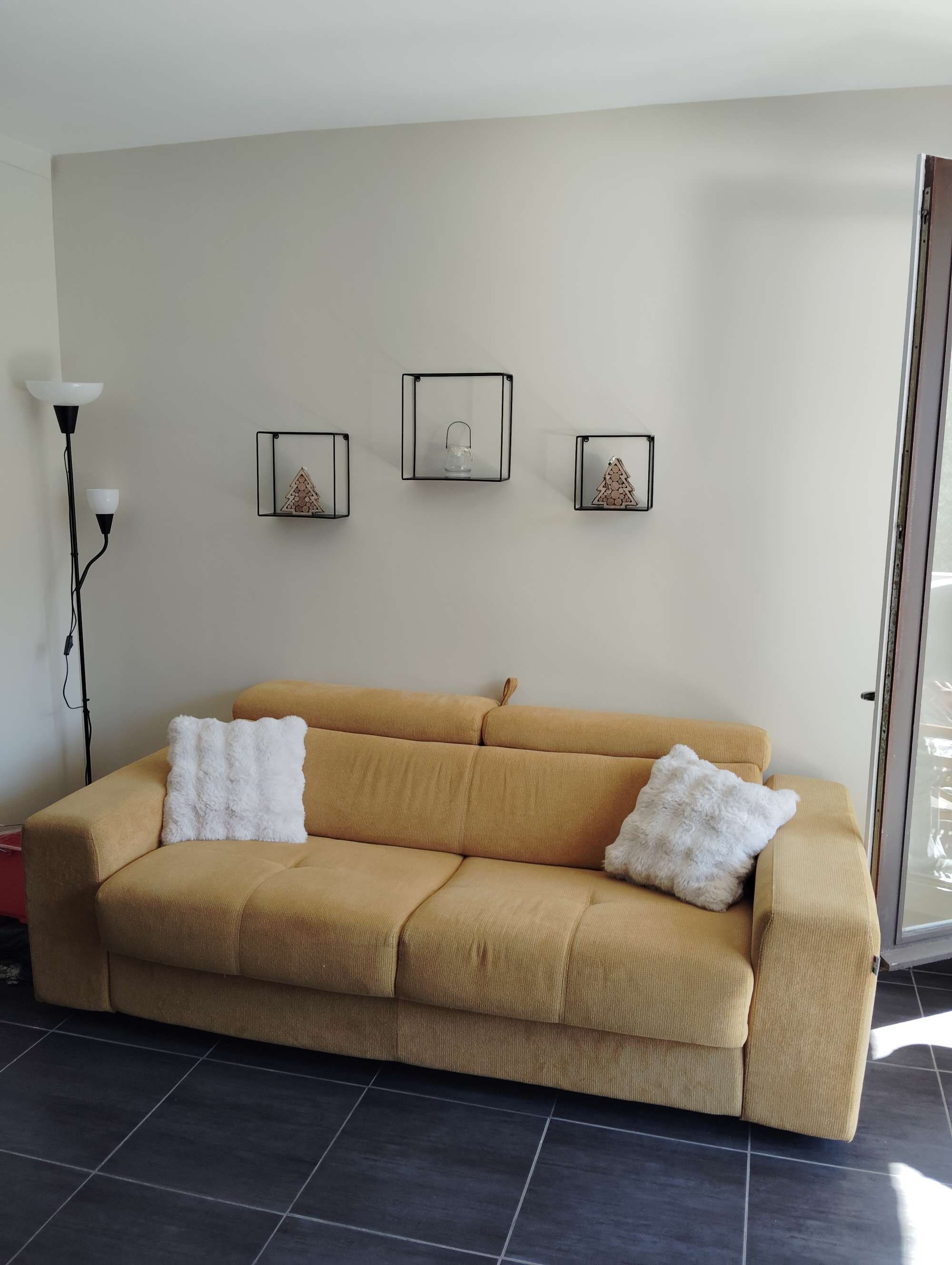 Ein Wohnzimmer mit einem beigen Sofa, zwei weißen, flauschigen Kissen und drei Wanddekorationen.