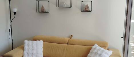 Ein Wohnzimmer mit einem beigen Sofa, zwei weißen, flauschigen Kissen und drei Wanddekorationen.