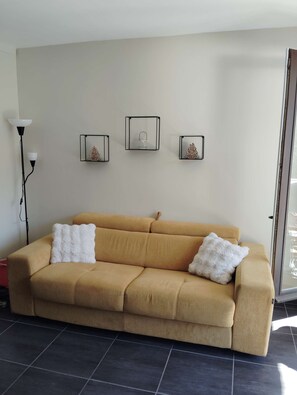 A living room with a beige sofa, two white fluffy cushions, and three wall-mounted decorations. - Studio Constellations d'Auron (Saint-Etienne-de-Tinée)