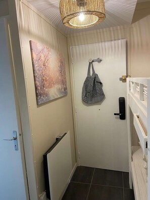 Un couloir avec une porte blanche, un sac suspendu, un tableau et un luminaire au plafond.