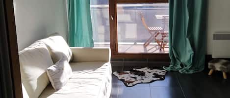 Una habitación con sofá, ventana con cortinas y vistas al exterior, además de una alfombra pequeña.