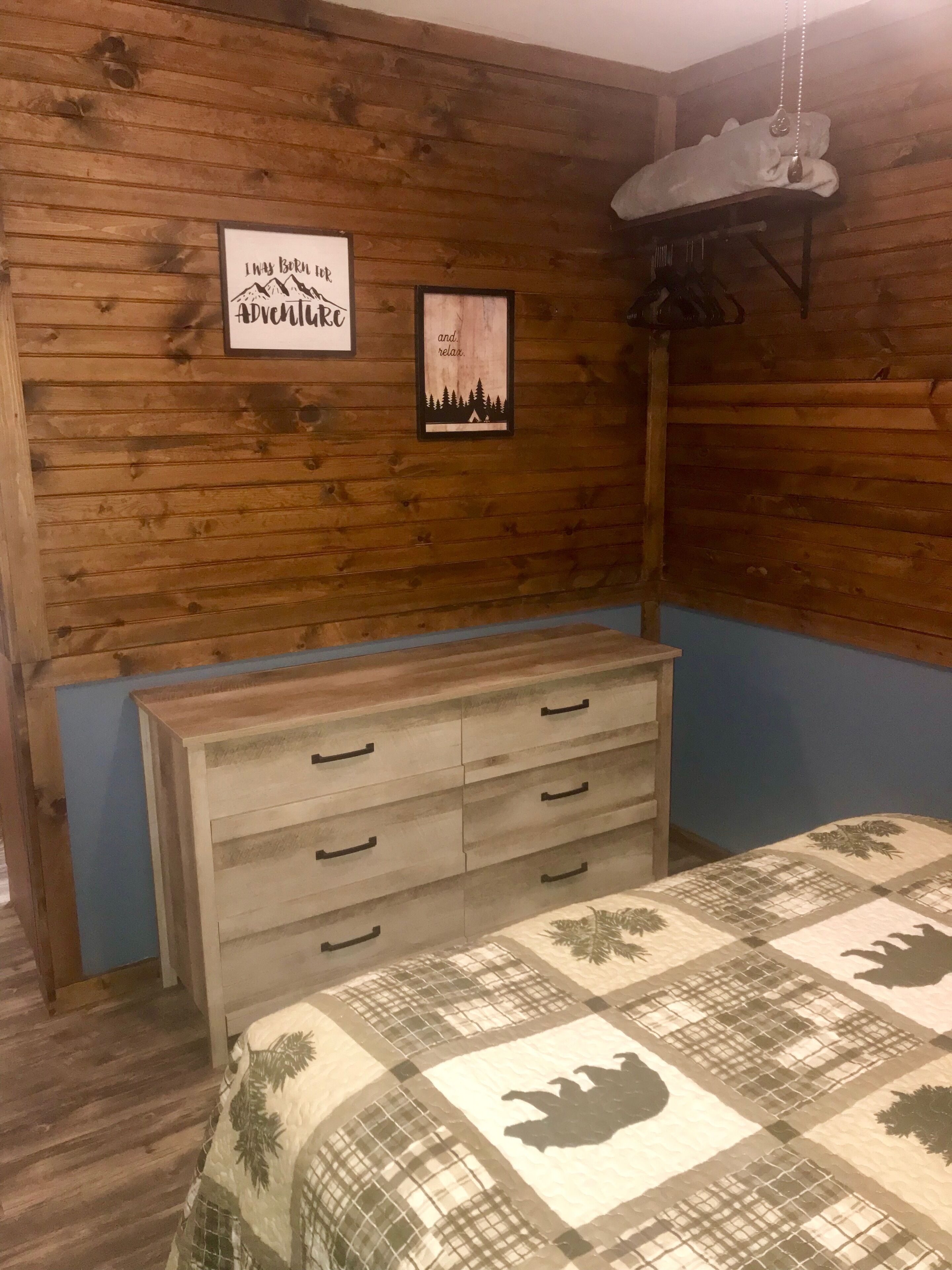 A wooden-paneled room with a bed, a dresser, and a wall-mounted shelf.