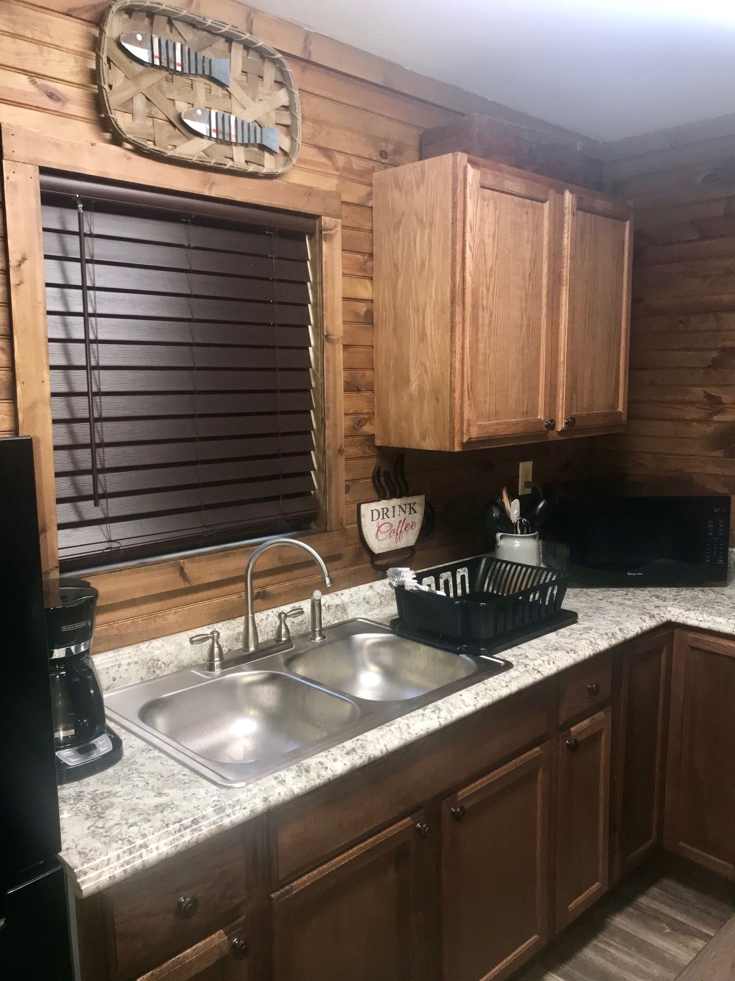 A kitchen with wooden cabinets, a double sink, and a coffee maker.