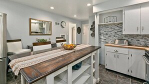 Una cocina moderna con una mesa de comedor de madera, armarios blancos y un salpicadero con baldosas grises.
