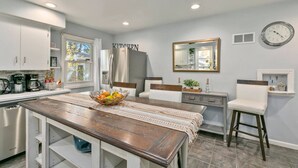 Una cocina moderna con una isla central, una zona de comedor con mesa de madera y una barra con una silla blanca.