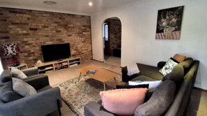 A living room with a brick wall, a flat-screen TV, a sofa, a coffee table, and a rug. - Coastal Getaway by Book Jervis Bay - Free Wifi, linen & Games Room (Huskisson)